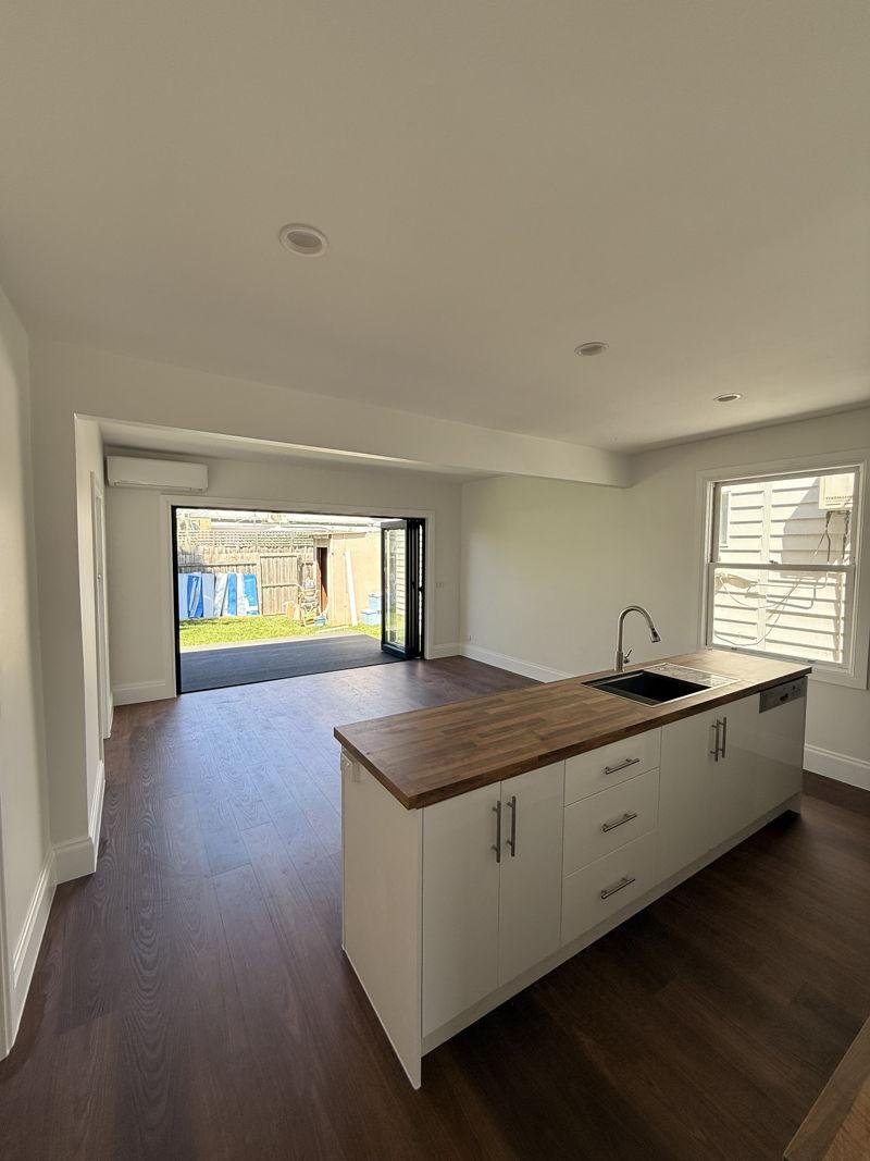 Renovated open-plan kitchen with a white island bench under a timber benchtop, dark timber floors and black-framed bifold doors open to the backyard