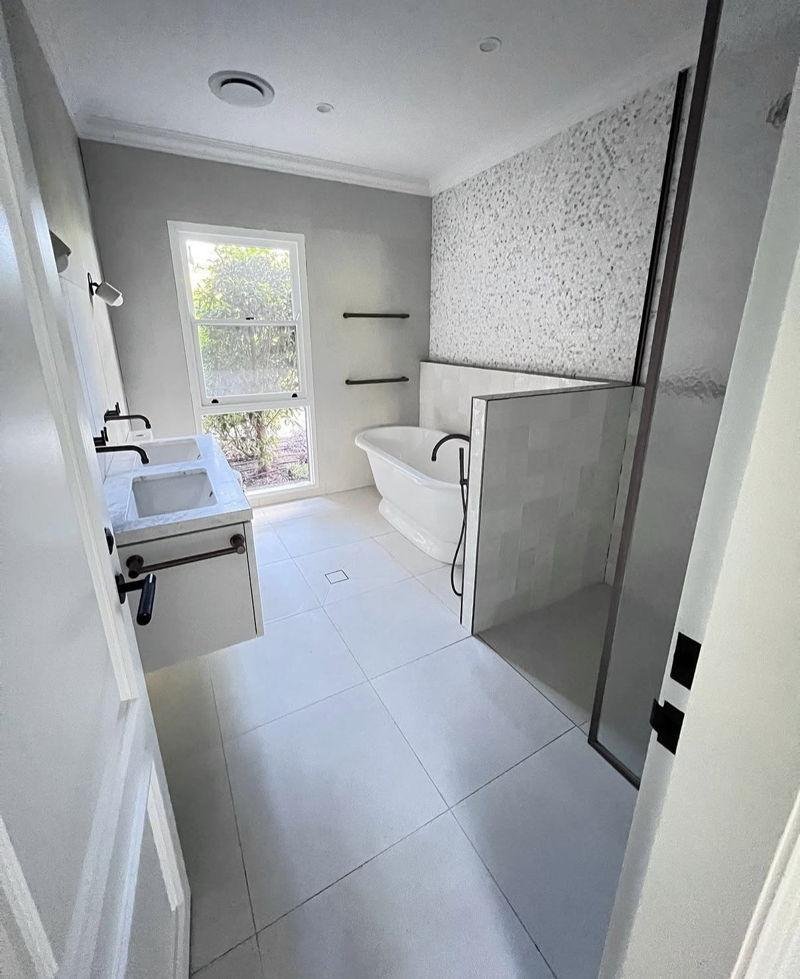 Finished bathroom with a freestanding bath, a half-height tiled wall to the shower, a double-basin wall-hung vanity, black tapware and large-format floor tiles