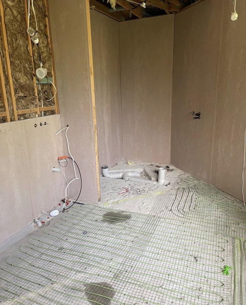 Bathroom stripped back to fibre cement sheeting, with plumbing roughed in and electric underfloor heating cable laid across the floor