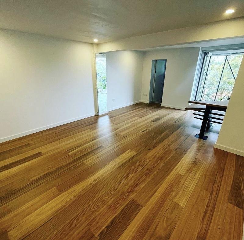 The same living area finished with wide timber floorboards, white walls, downlights and glass doors out to the garden