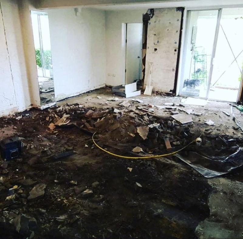 Living area mid-demolition, the floor dug out to dirt and rubble, with a wall opened up between the doorways
